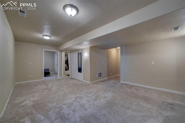 basement featuring light carpet and a textured ceiling