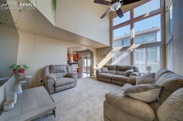 living room featuring ceiling fan with notable chandelier, a towering ceiling, and carpet