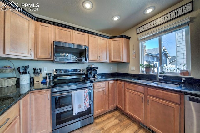 kitchen featuring sink, a textured ceiling, appliances with stainless steel finishes, dark stone countertops, and light hardwood / wood-style floors