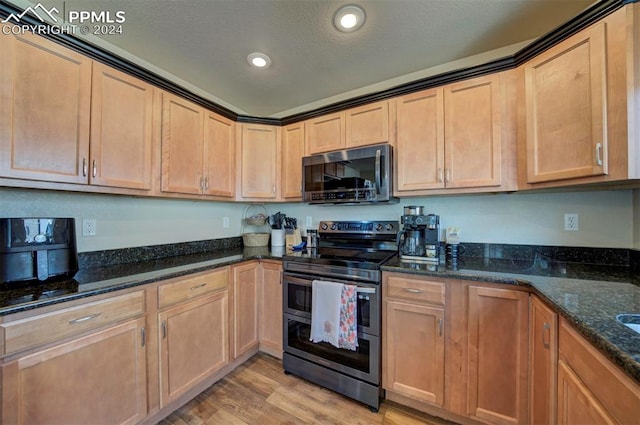 kitchen with stainless steel appliances, dark stone countertops, and light wood-type flooring