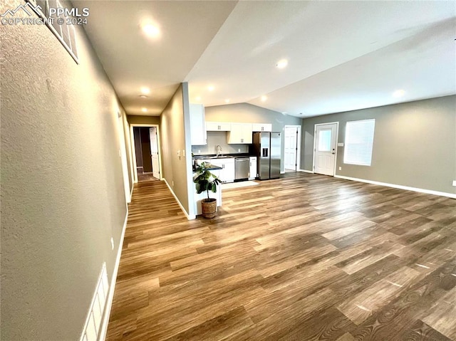 unfurnished living room with lofted ceiling, sink, and light hardwood / wood-style flooring