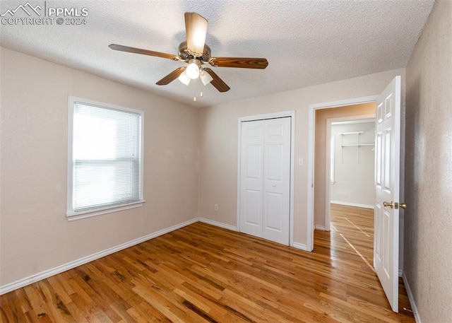 unfurnished bedroom with a textured ceiling, a closet, light hardwood / wood-style flooring, and ceiling fan