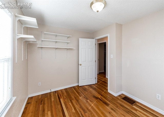 empty room with a textured ceiling, hardwood / wood-style flooring, and plenty of natural light