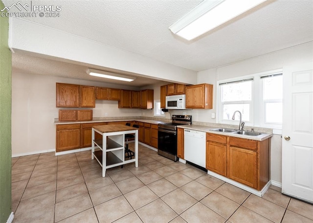 kitchen with a textured ceiling, sink, light tile patterned floors, and white appliances