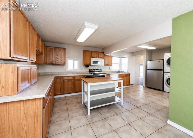 kitchen with sink, stainless steel appliances, light tile patterned floors, stacked washer and dryer, and a kitchen island