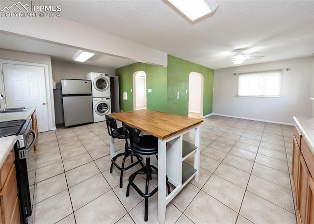 kitchen with stacked washer and clothes dryer, ceiling fan, a textured ceiling, light tile patterned flooring, and stainless steel appliances