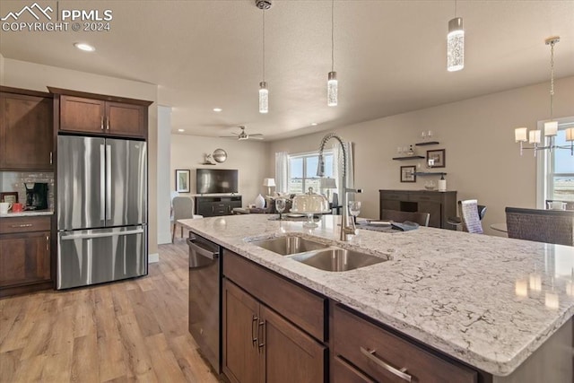 kitchen featuring light wood-type flooring, sink, ceiling fan with notable chandelier, pendant lighting, and appliances with stainless steel finishes