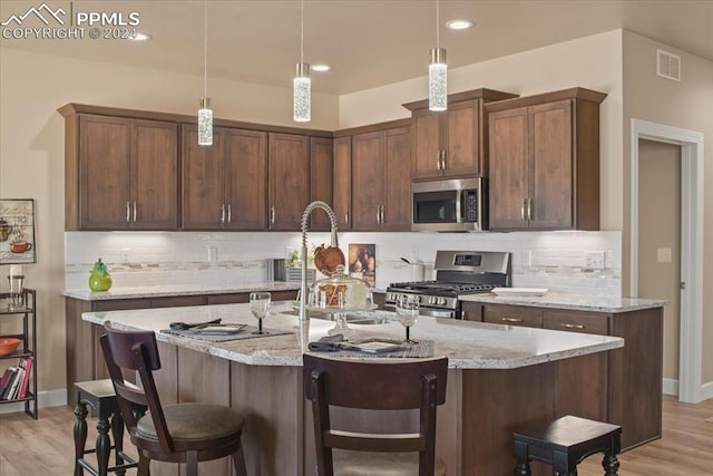 kitchen featuring light stone counters, hanging light fixtures, appliances with stainless steel finishes, and light wood-type flooring