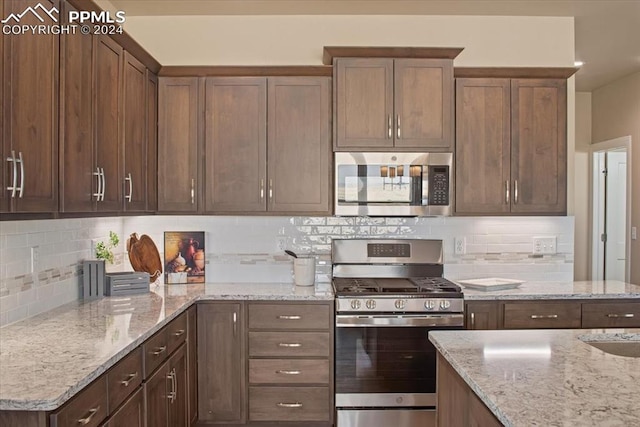 kitchen with appliances with stainless steel finishes, light stone counters, and decorative backsplash