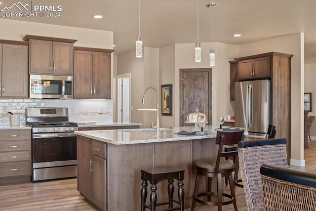 kitchen featuring light hardwood / wood-style floors, decorative light fixtures, a center island with sink, stainless steel appliances, and backsplash