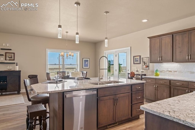 kitchen with stainless steel dishwasher, sink, light hardwood / wood-style floors, pendant lighting, and a center island with sink