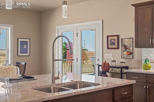 kitchen with dark brown cabinetry, pendant lighting, light stone countertops, and sink