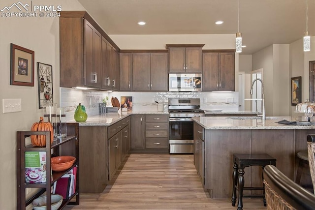 kitchen featuring stainless steel appliances, light stone countertops, decorative light fixtures, and light hardwood / wood-style flooring