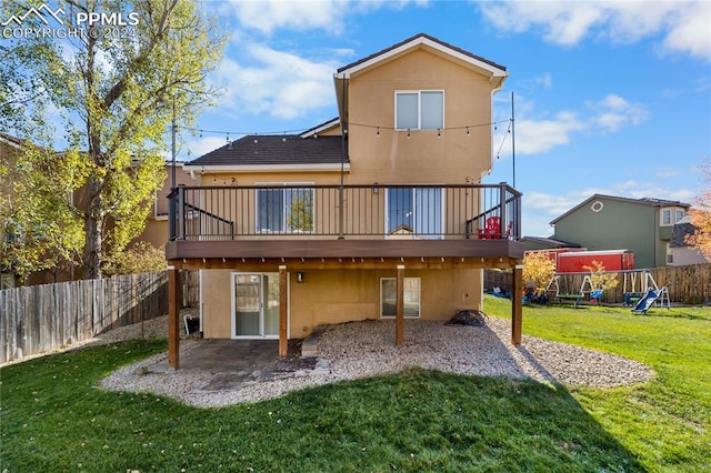 back of property featuring a wooden deck, a patio area, a lawn, and a playground