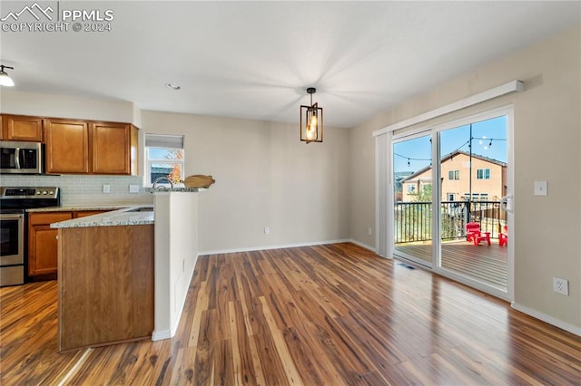 kitchen with hanging light fixtures, backsplash, light stone countertops, dark hardwood / wood-style floors, and stainless steel appliances