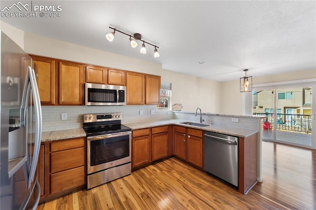 kitchen with sink, kitchen peninsula, stainless steel appliances, pendant lighting, and light hardwood / wood-style flooring