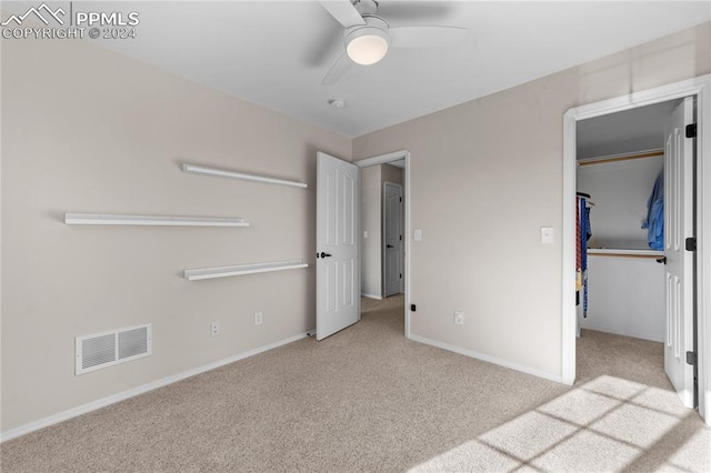 unfurnished bedroom with a walk in closet, light colored carpet, a closet, and ceiling fan