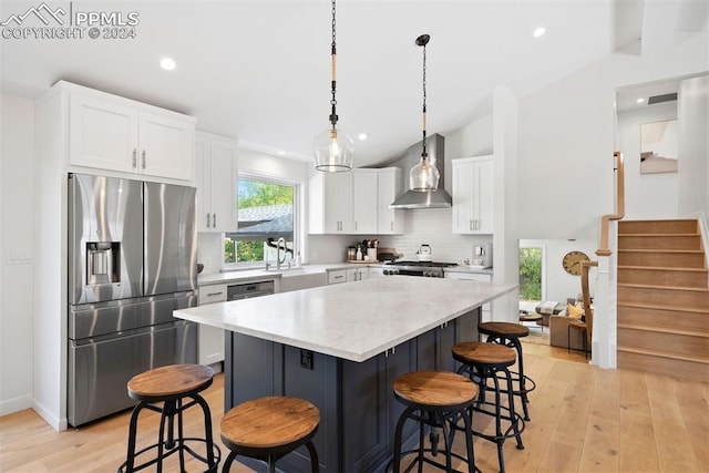 kitchen with white cabinets, wall chimney exhaust hood, vaulted ceiling, light hardwood / wood-style flooring, and appliances with stainless steel finishes