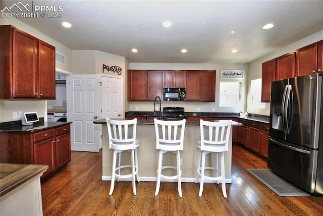 kitchen with a breakfast bar area, a kitchen island with sink, dark hardwood / wood-style flooring, and black appliances