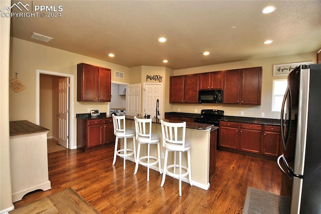 kitchen featuring a center island with sink, black appliances, a breakfast bar area, and dark hardwood / wood-style flooring