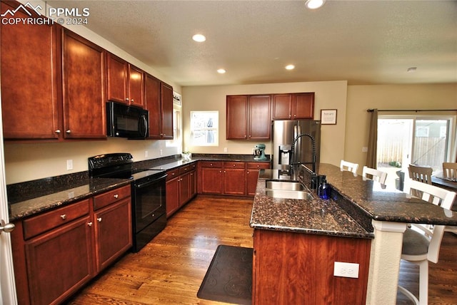 kitchen featuring black appliances, a kitchen island with sink, dark hardwood / wood-style floors, sink, and a breakfast bar area