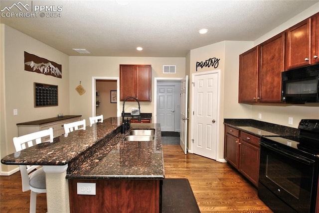 kitchen with hardwood / wood-style floors, dark stone countertops, a center island with sink, sink, and black appliances