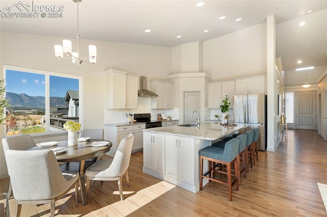 kitchen featuring an island with sink, stainless steel fridge, white cabinets, black / electric stove, and high vaulted ceiling