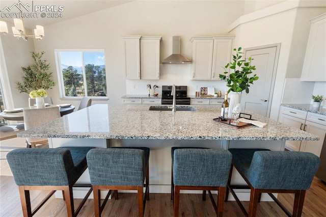 kitchen with wall chimney exhaust hood, lofted ceiling, light wood-type flooring, and a kitchen island with sink