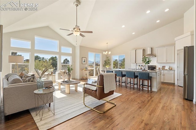 living room with light hardwood / wood-style floors, high vaulted ceiling, sink, and ceiling fan with notable chandelier