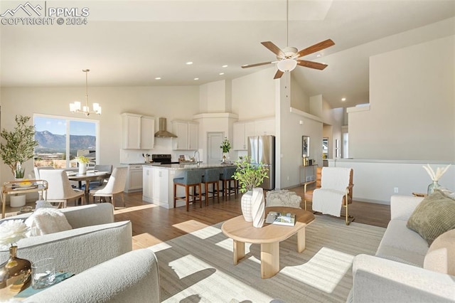 living room with light hardwood / wood-style floors, high vaulted ceiling, sink, and ceiling fan with notable chandelier