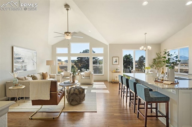 living room featuring a wealth of natural light, ceiling fan with notable chandelier, wood-type flooring, and high vaulted ceiling