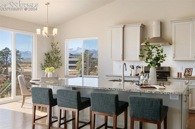 kitchen with wall chimney exhaust hood, white cabinetry, light wood-type flooring, and a wealth of natural light