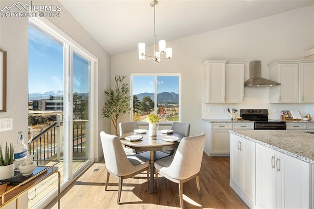 dining space with a mountain view, vaulted ceiling, light wood-type flooring, and an inviting chandelier