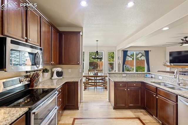 kitchen with decorative light fixtures, stainless steel appliances, sink, and light hardwood / wood-style flooring