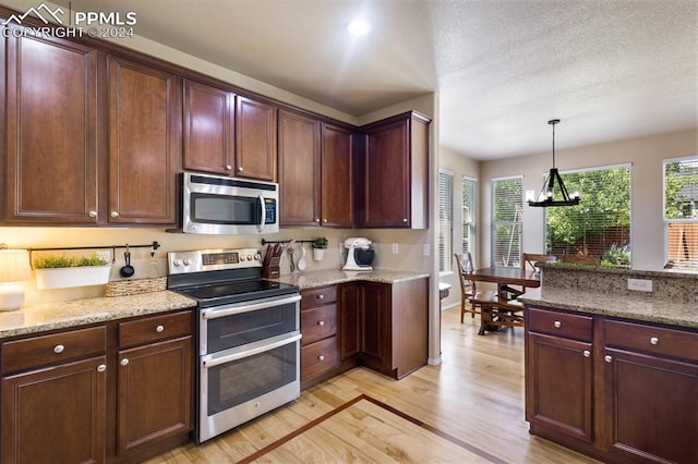 kitchen with stainless steel appliances, light hardwood / wood-style floors, an inviting chandelier, and light stone counters