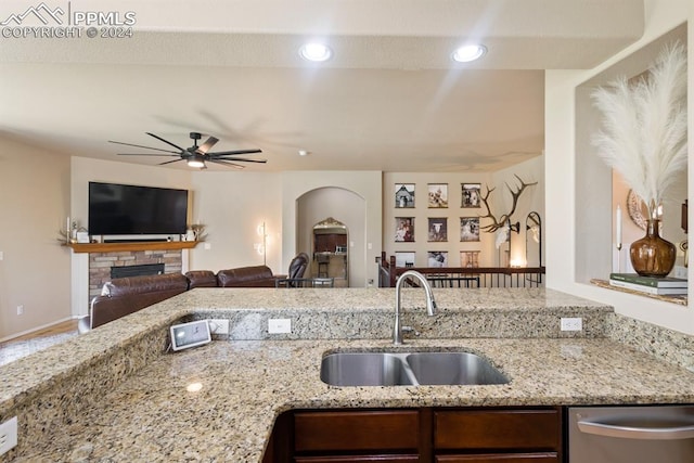 kitchen with ceiling fan, sink, a fireplace, light stone countertops, and dishwasher