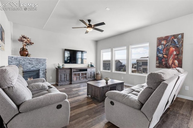 living room featuring a stone fireplace, dark wood-type flooring, and ceiling fan