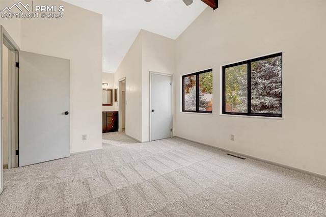 unfurnished bedroom with high vaulted ceiling, ensuite bathroom, and light carpet