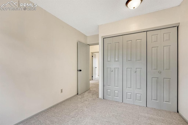 unfurnished bedroom featuring a textured ceiling, a closet, and light colored carpet