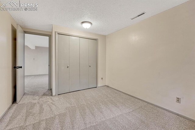 unfurnished bedroom featuring light colored carpet, a textured ceiling, and a closet