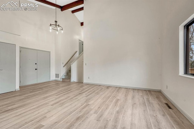 unfurnished living room with high vaulted ceiling, beamed ceiling, an inviting chandelier, and light hardwood / wood-style floors