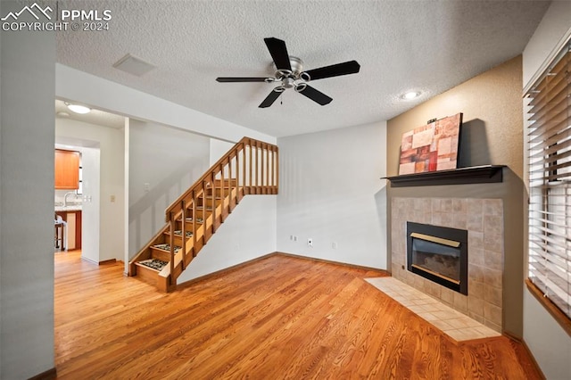 living room with a textured ceiling, a tiled fireplace, and light wood-type flooring