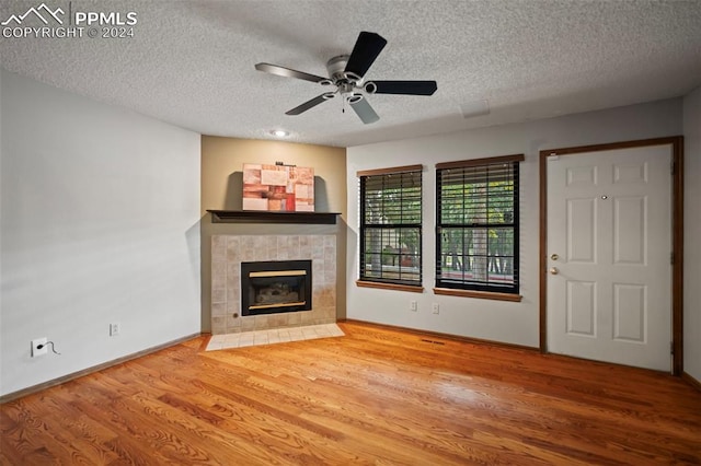 unfurnished living room with a textured ceiling, wood-type flooring, a tile fireplace, and ceiling fan