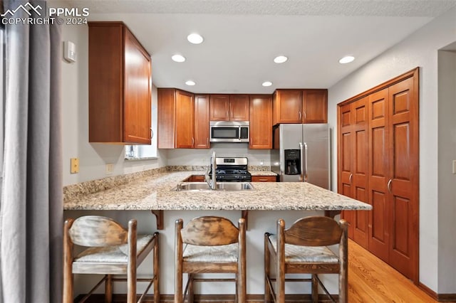 kitchen featuring sink, light stone countertops, a kitchen bar, light wood-type flooring, and appliances with stainless steel finishes