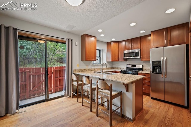 kitchen featuring light stone countertops, appliances with stainless steel finishes, sink, kitchen peninsula, and light hardwood / wood-style floors