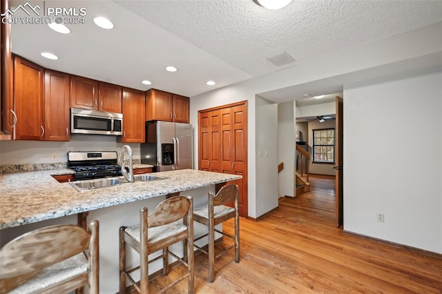 kitchen featuring kitchen peninsula, ceiling fan, appliances with stainless steel finishes, a breakfast bar, and light hardwood / wood-style flooring