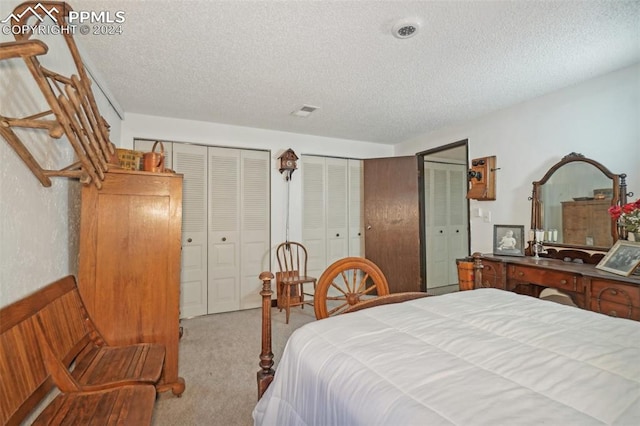 bedroom featuring light carpet, two closets, and a textured ceiling