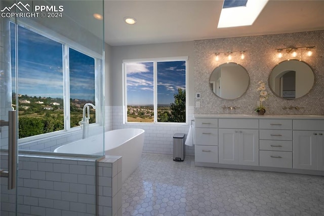 bathroom with a skylight, a wealth of natural light, vanity, and tiled bath