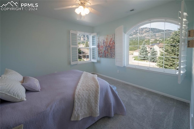 bedroom featuring a mountain view, carpet flooring, multiple windows, and ceiling fan