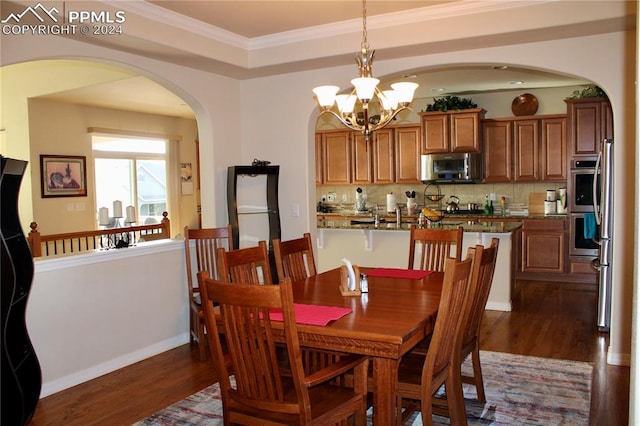 dining area featuring arched walkways, dark wood-style flooring, a notable chandelier, crown molding, and baseboards